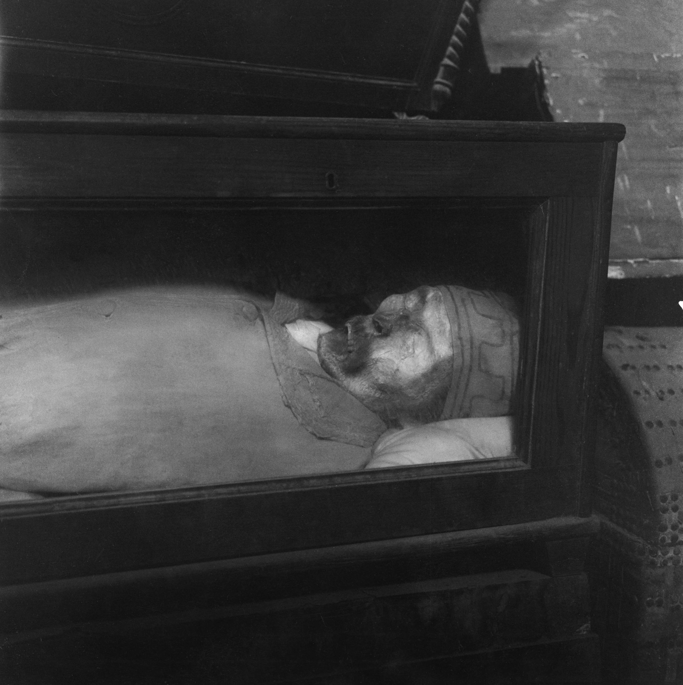 Black and white photograph of a corpse with a skullcap inside a coffin