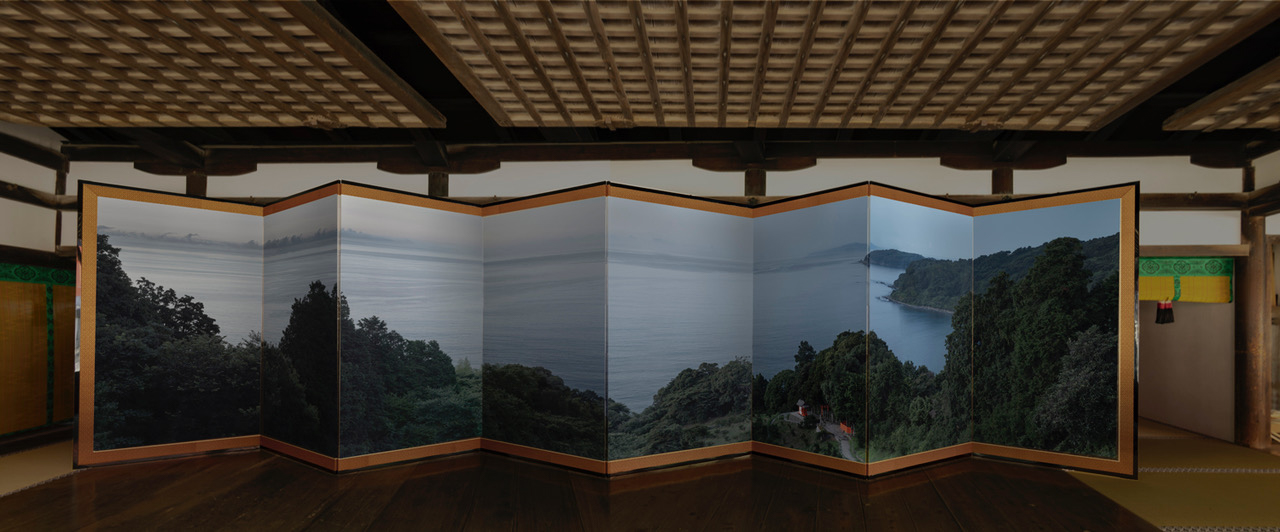 Installation view of a color photograph depicting a landscape mounted on a folding screen
