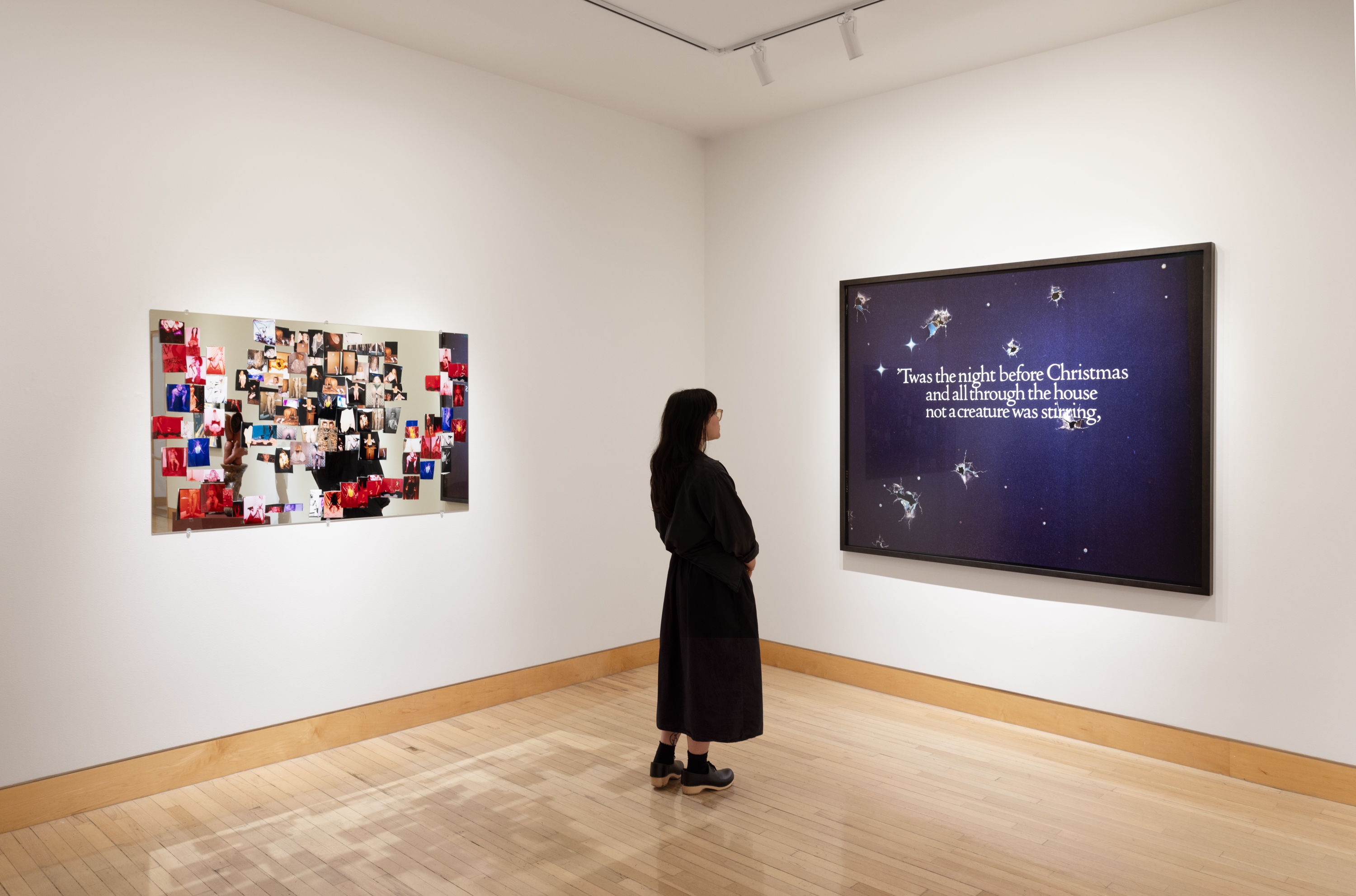 Color image of a figure looking at a large color photograph framed in black on a white wall