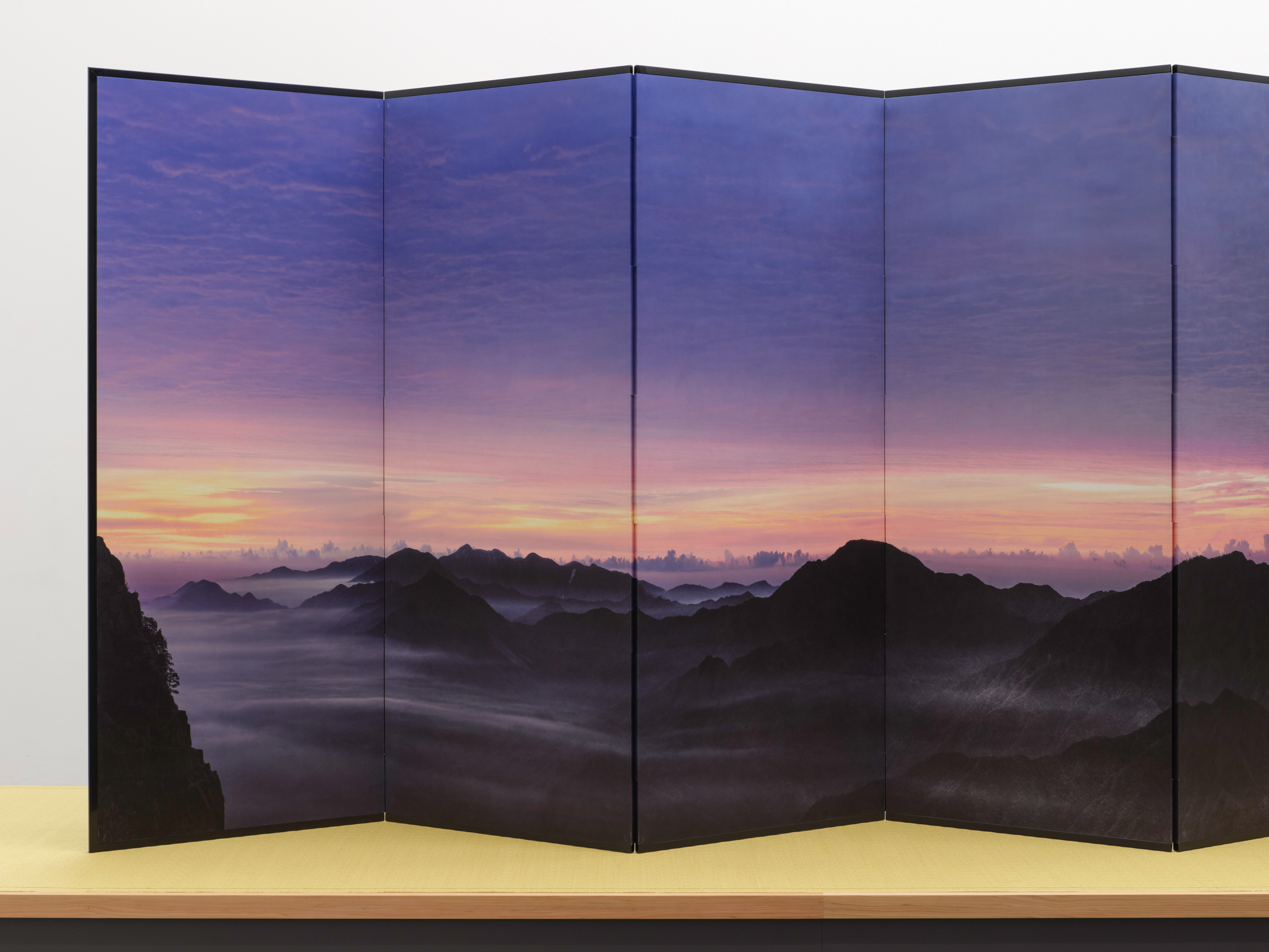 An instillation shot of a folding screen depicting a landscape at sunset on the screen