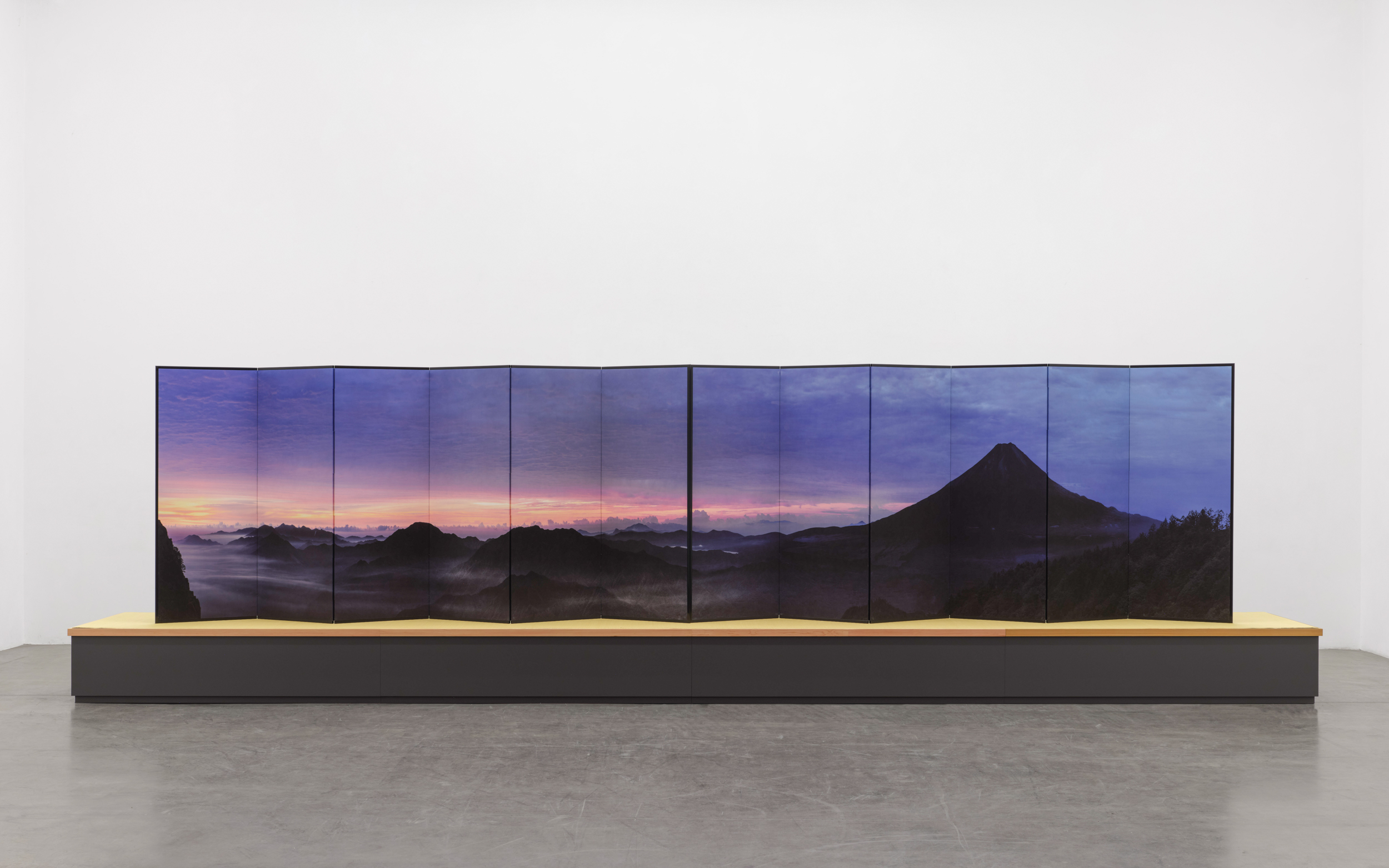 Installation view of a long folding screen depicting Mt. Fuji; the screen sits on a large pedestal