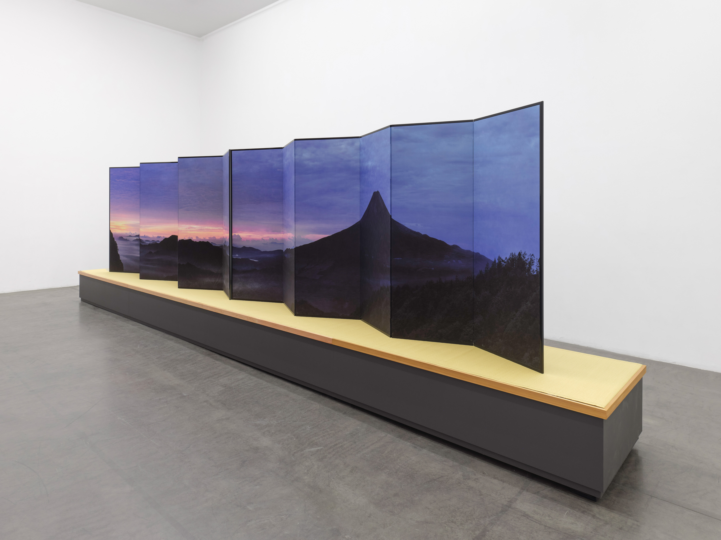 Installation view of a long folding screen depicting Mt. Fuji; the screen sits on a large pedestal
