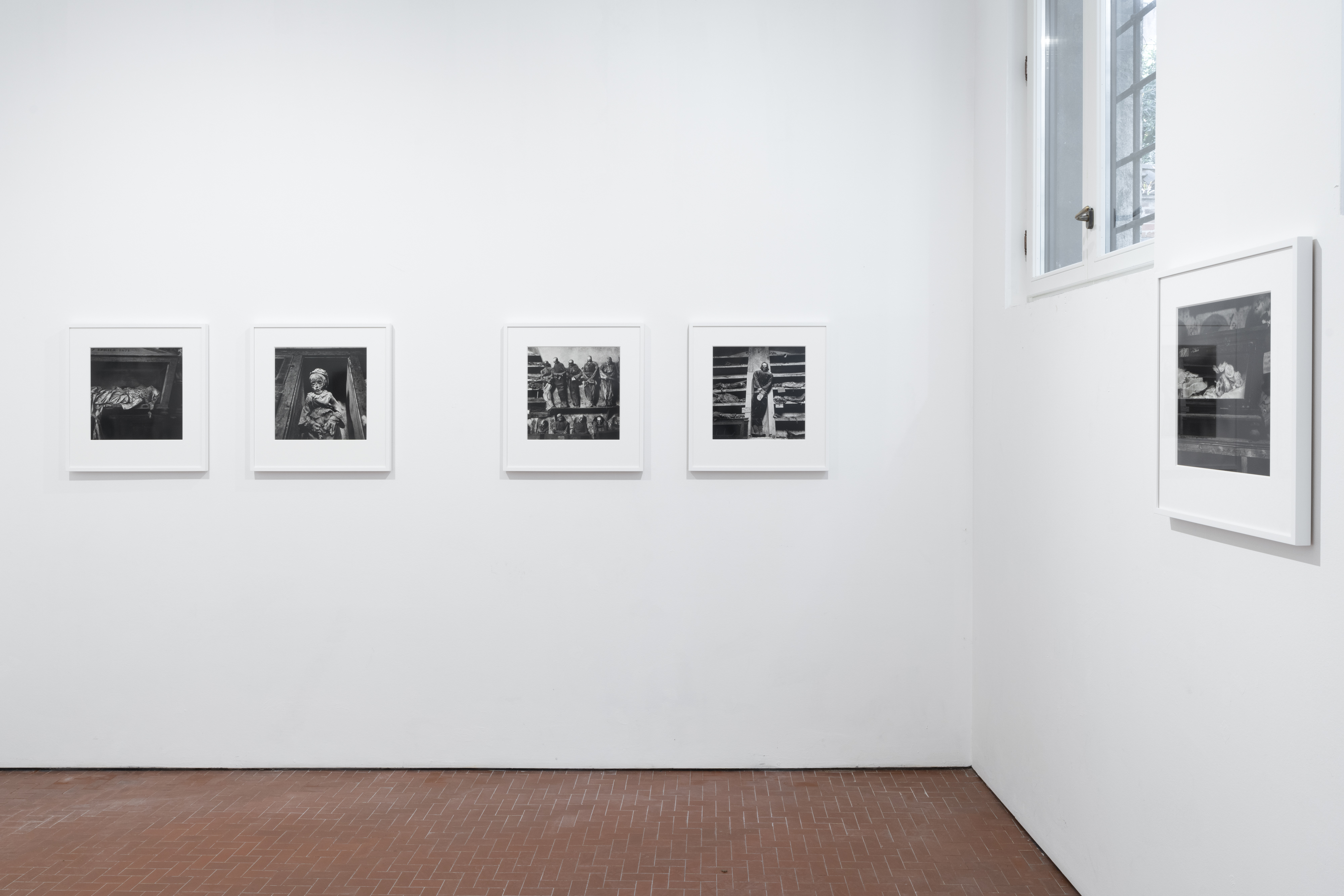 Color image of an exhibition of black and white photographs depicting various portraits framed in white on white walls