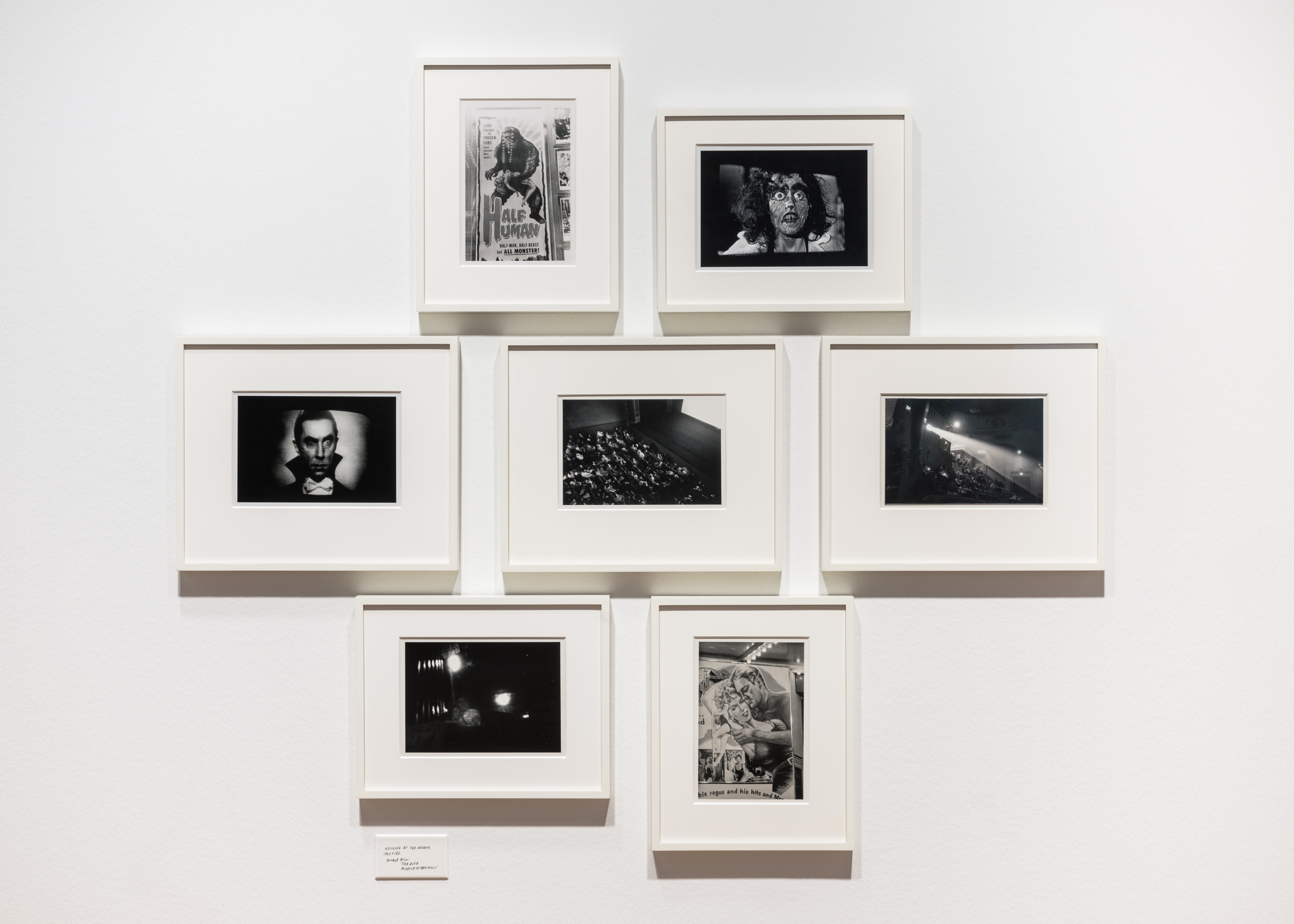 Color image of a suite of seven black and white photographs framed in white on white wall