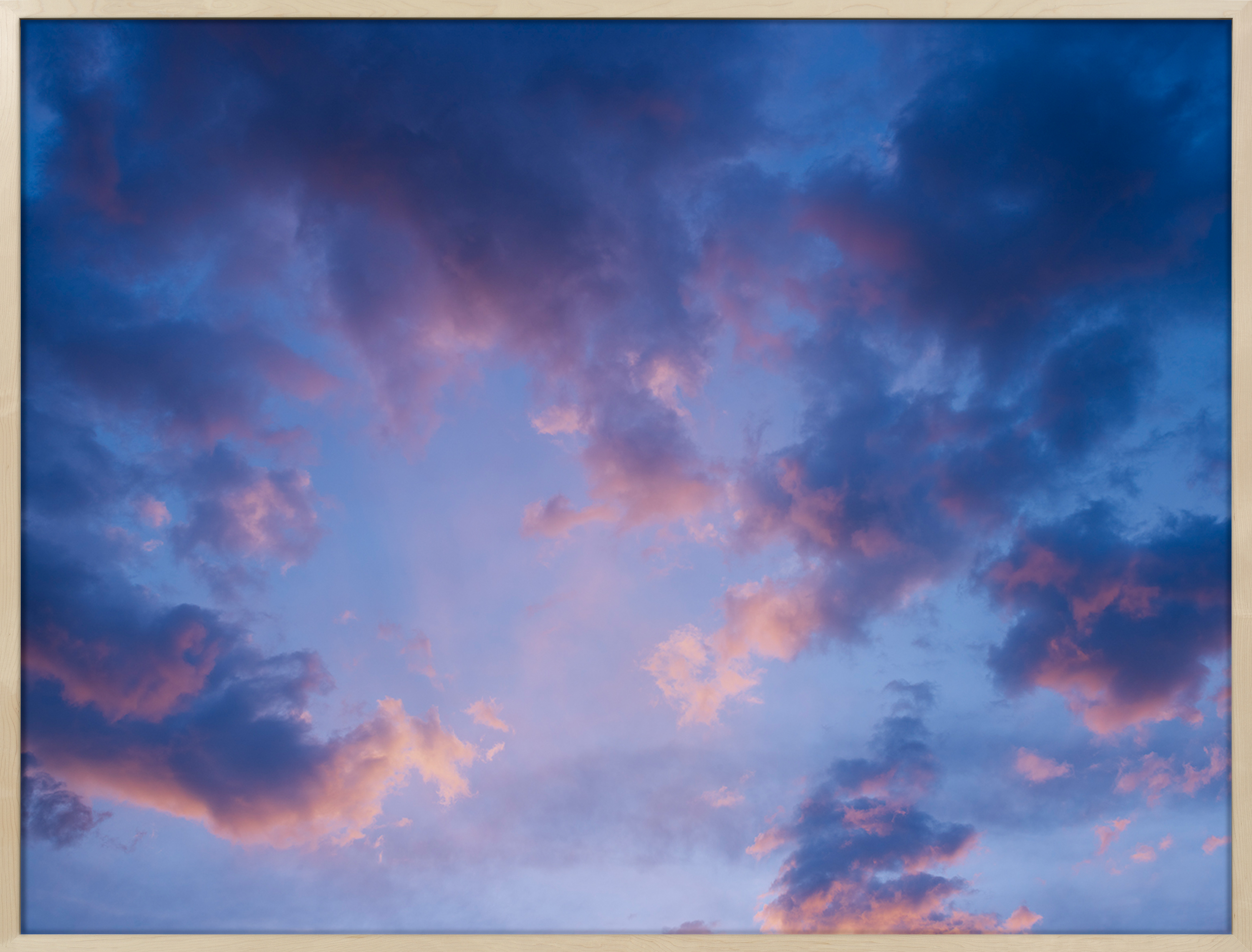 Color photograph of the sky with clouds in shades of blue, purple, and pink framed in wood