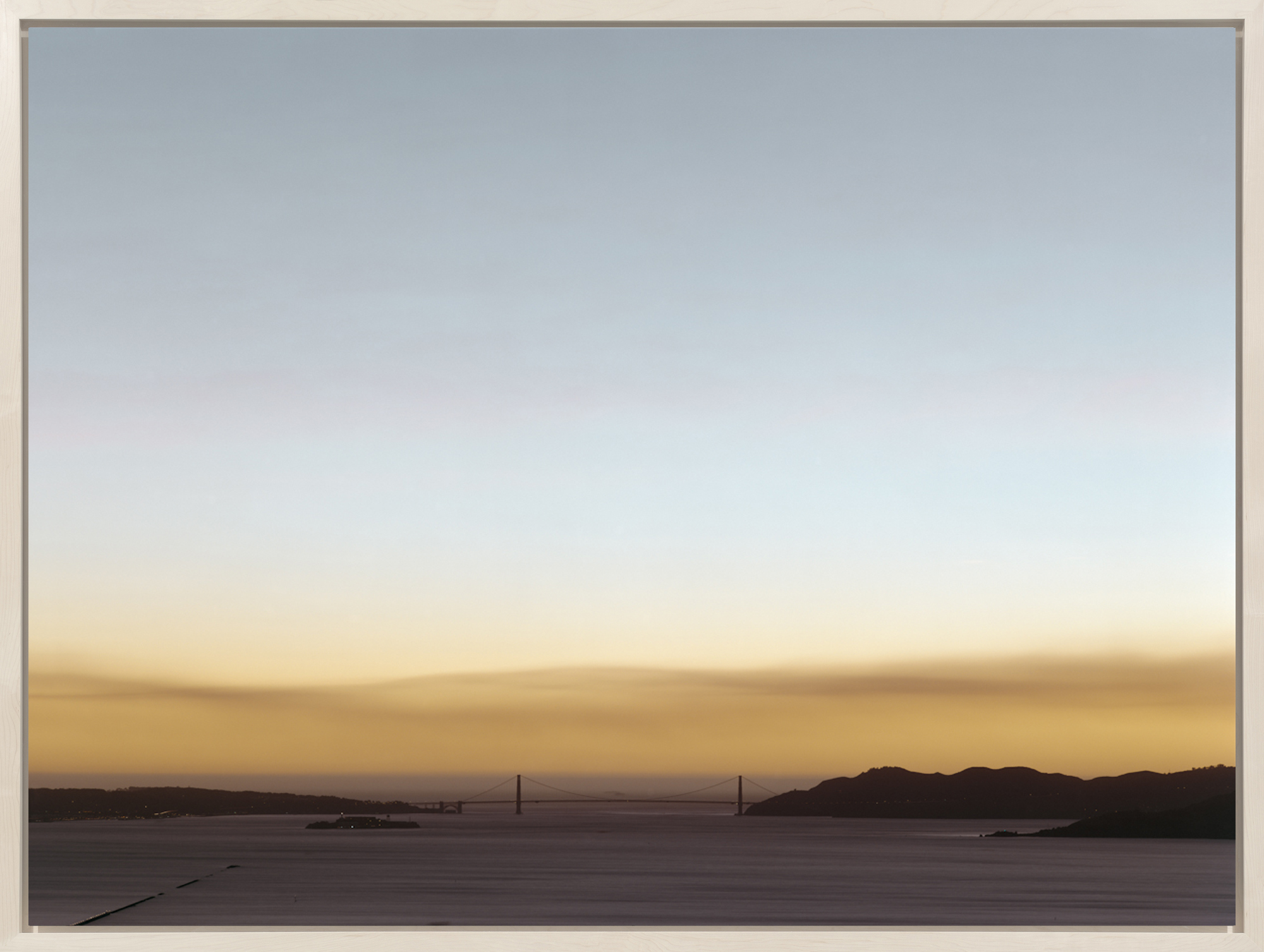 Color photograph of the Golden Gate bridge surrounded by the bay during sunset with wildfire smoke in the air framed in light wood