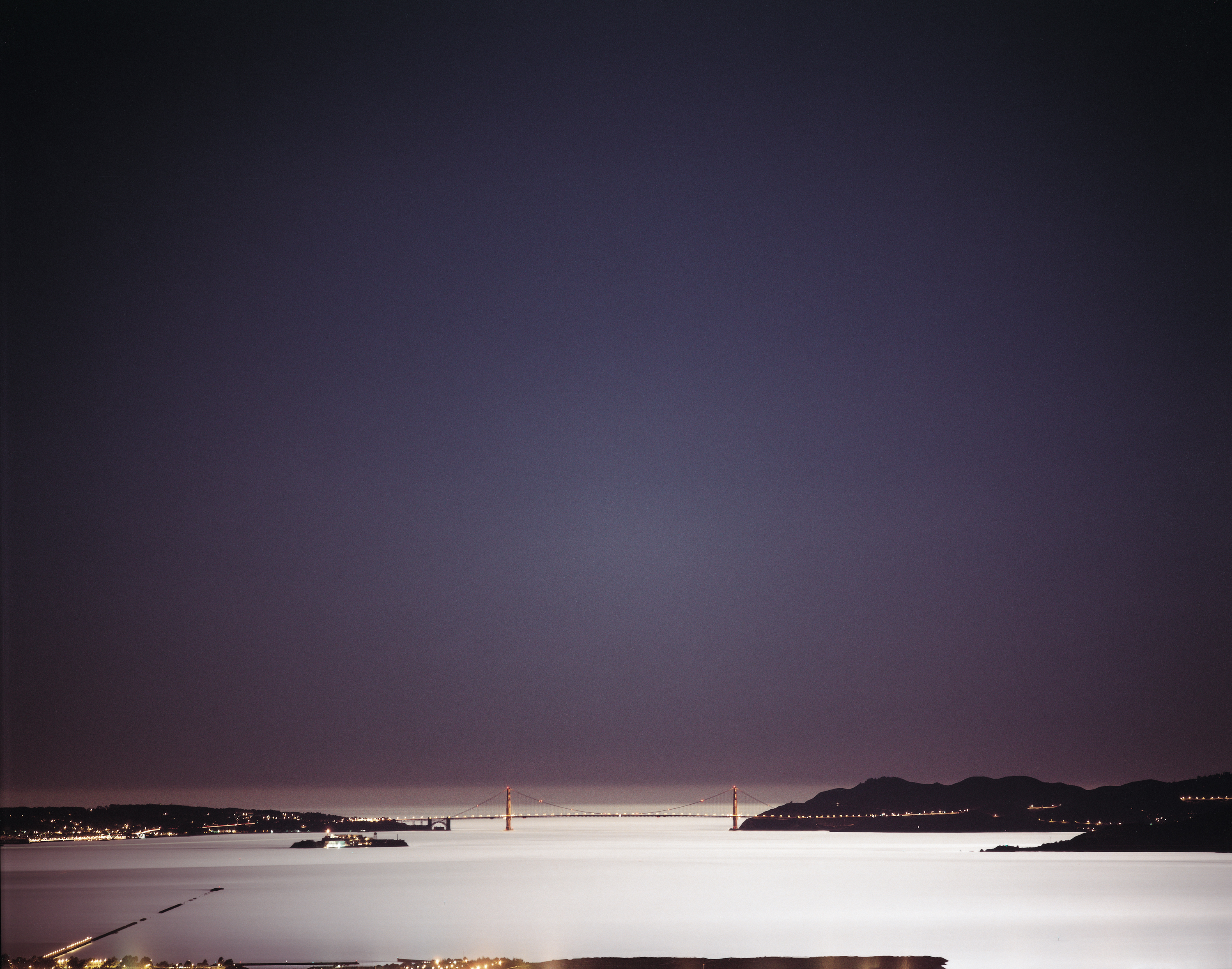 Color photograph of the Golden Gate bridge and surrounding bay late at night and early morning