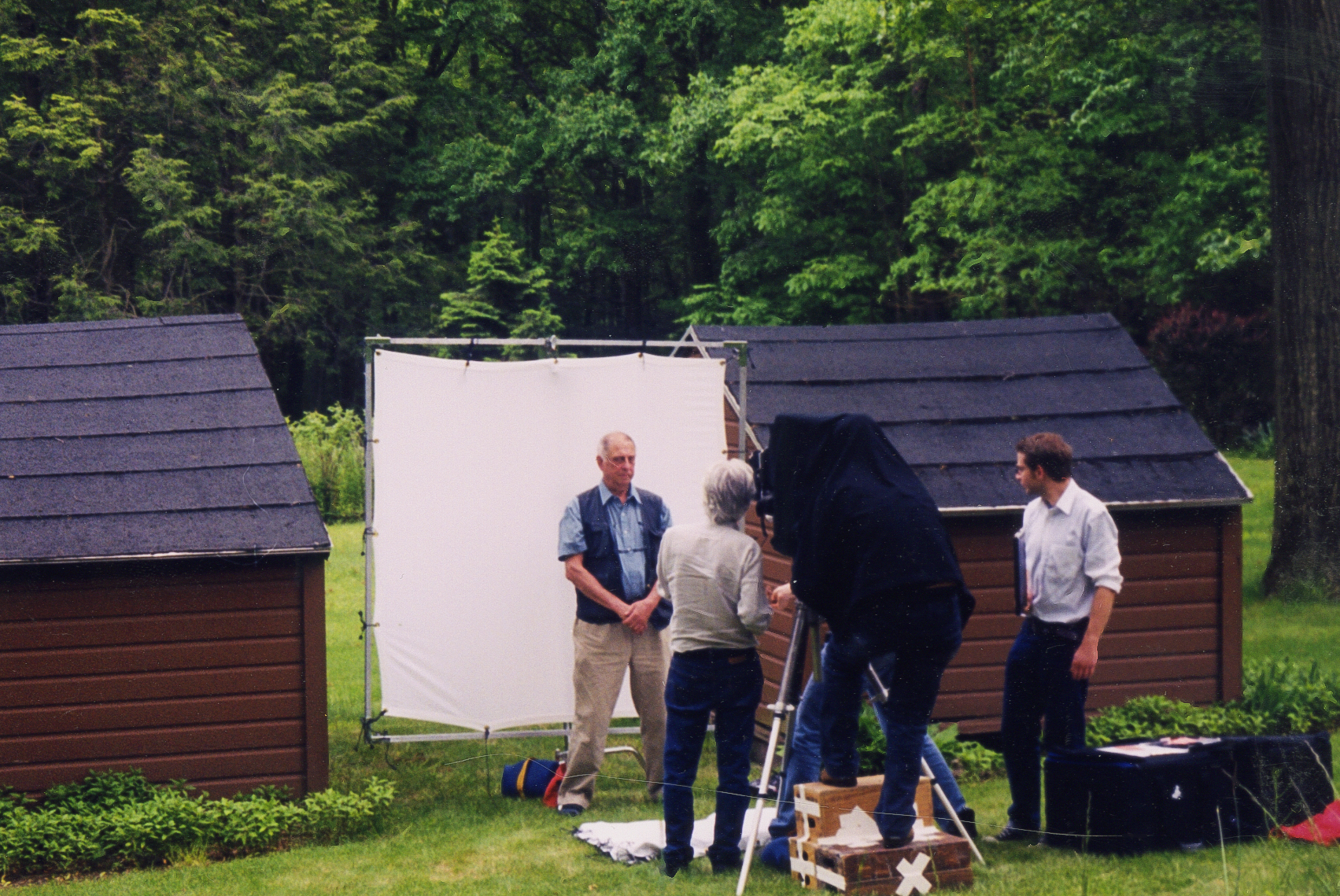 Color photograph of four figures one taking a photograph of the other outdoors in a verdant field