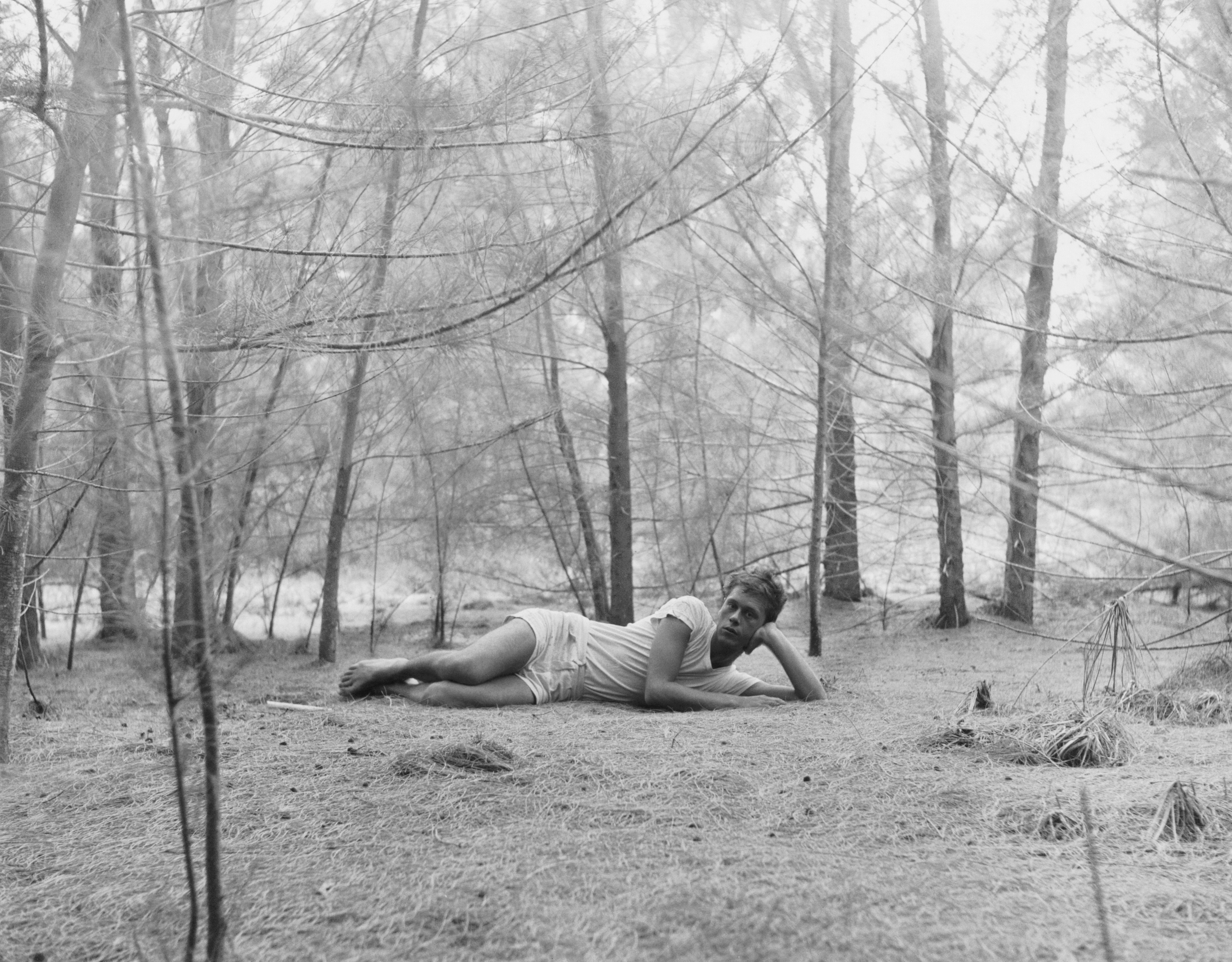 Black and white photograph of a figure laying down in the middle of a forest