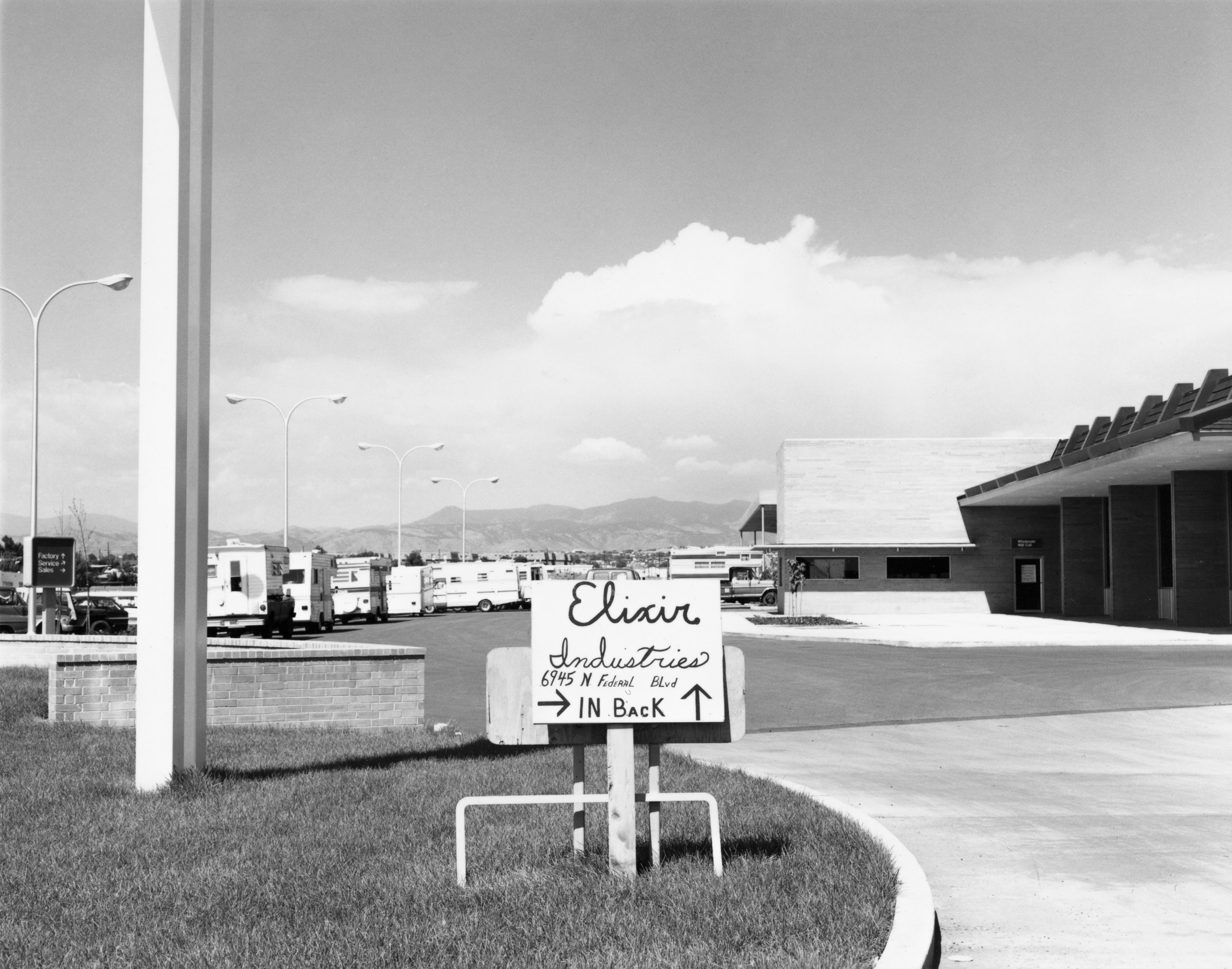 Black and white photograph of the exterior of a parking lot with a sign reading elixir industries