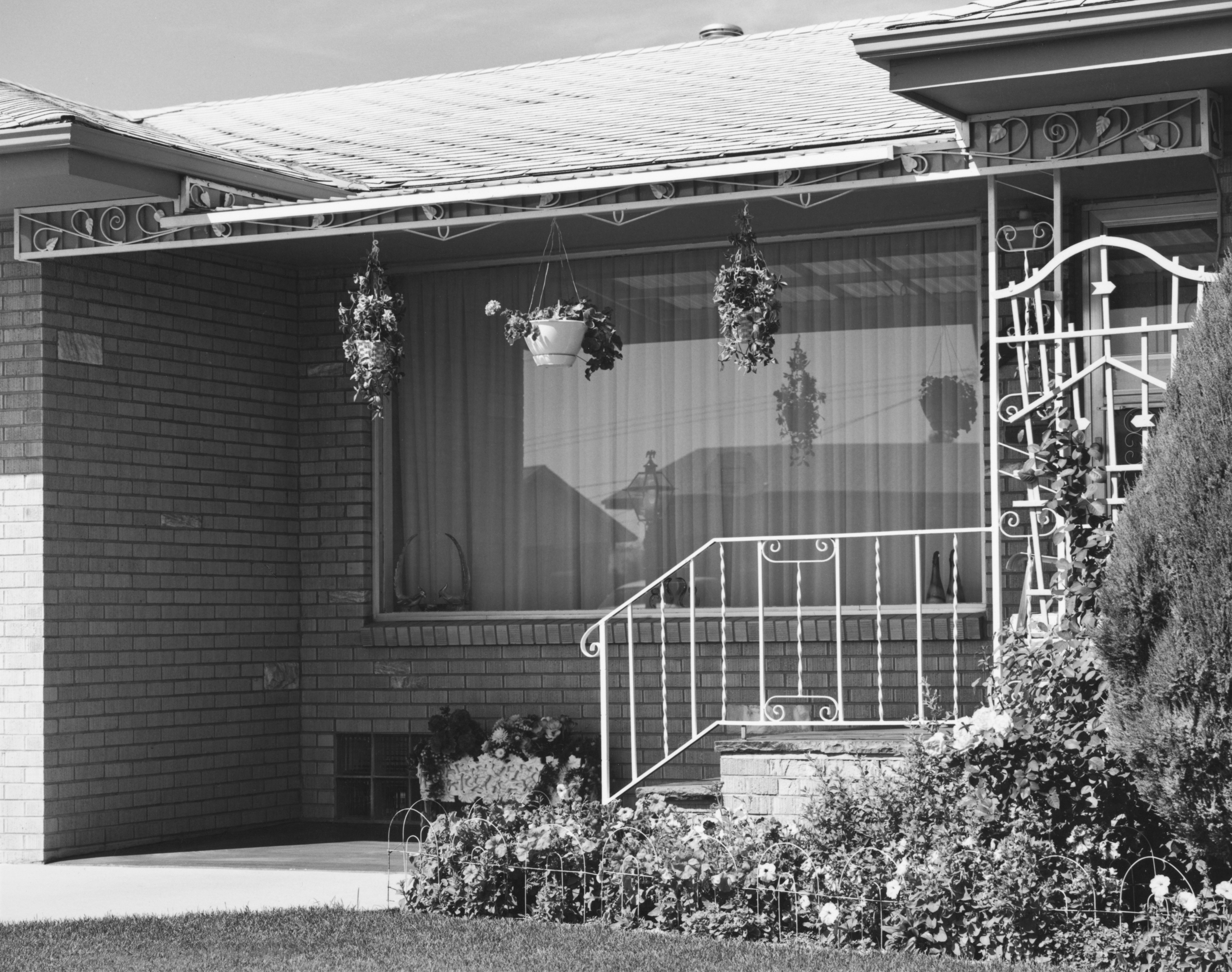 Black and white photograph of the exterior of a home with three hanging plants