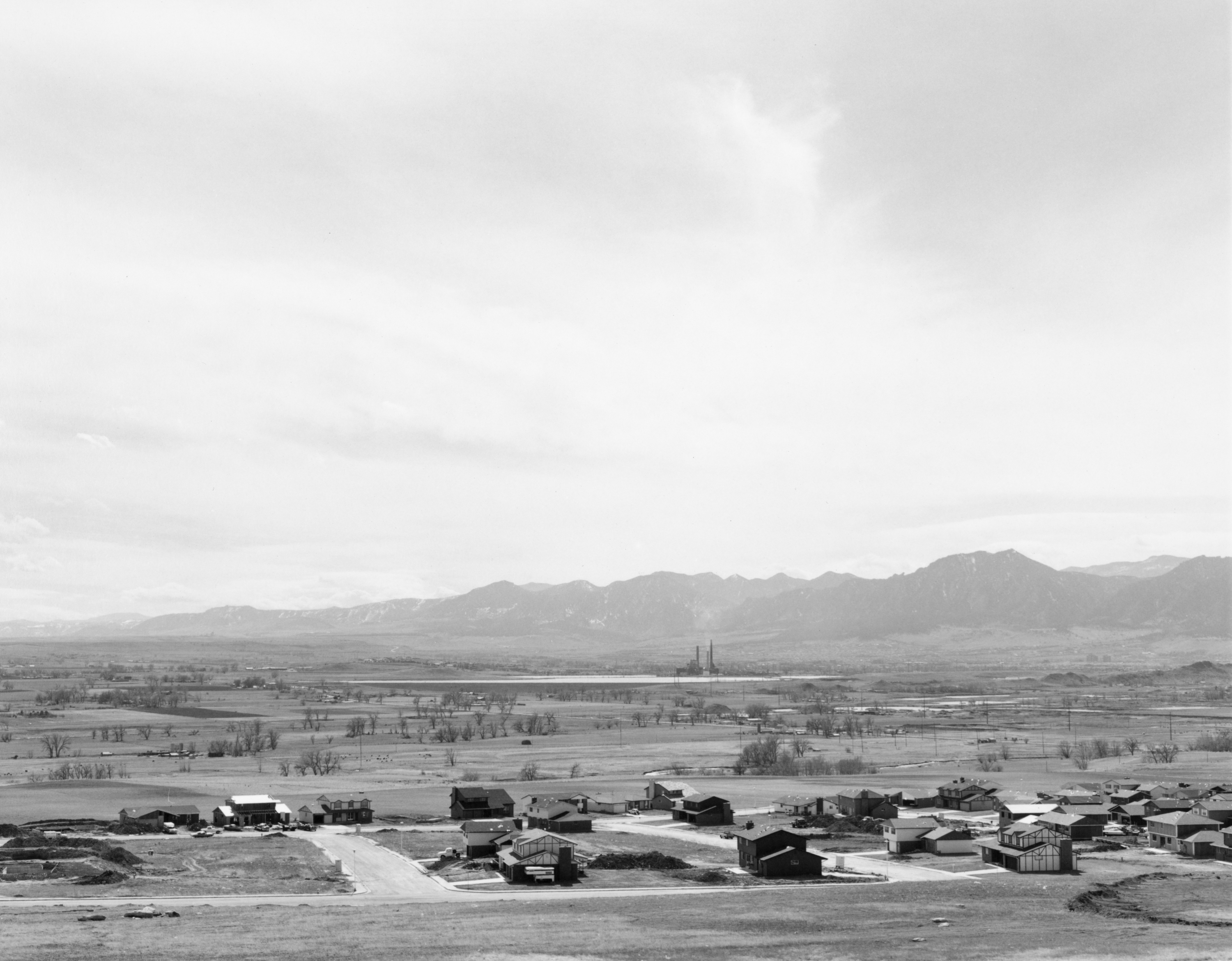 Black and white photograph of a newly developed residential area amongst a mountain range and power plant