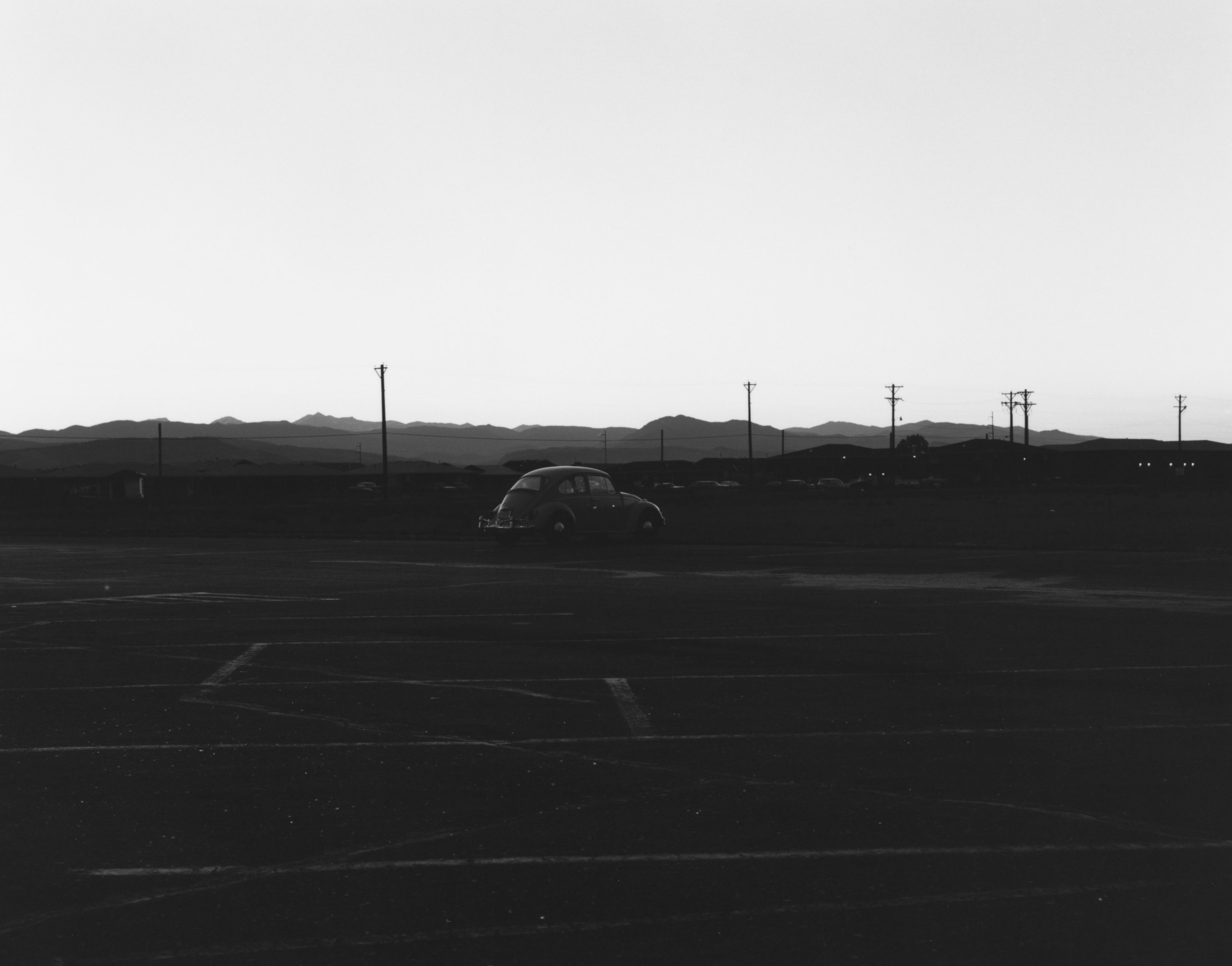 Black and white photograph of a Volkswagen beetle in an empty parking lot