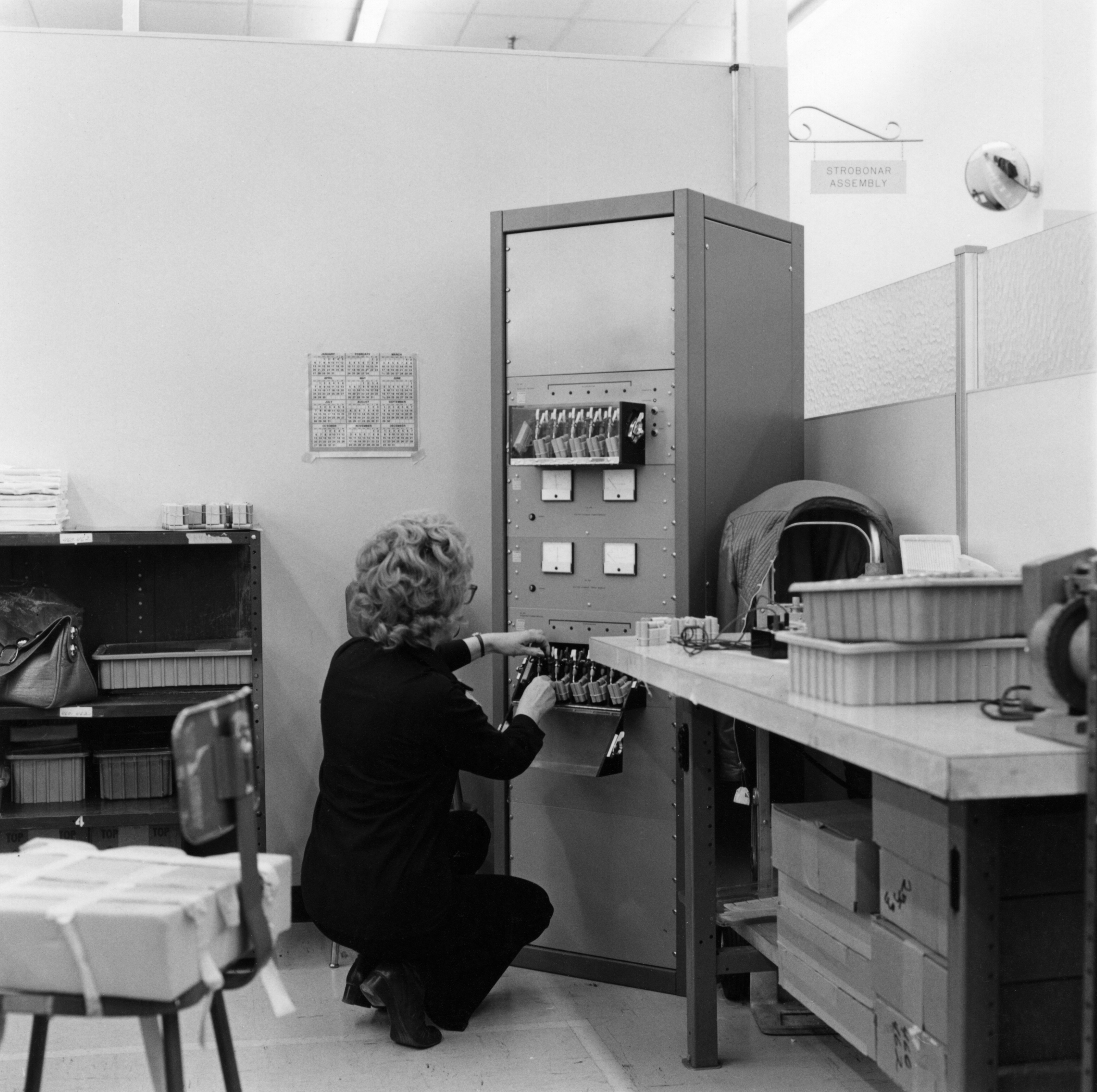 Black and white photograph of a kneeling figure in front of a machine