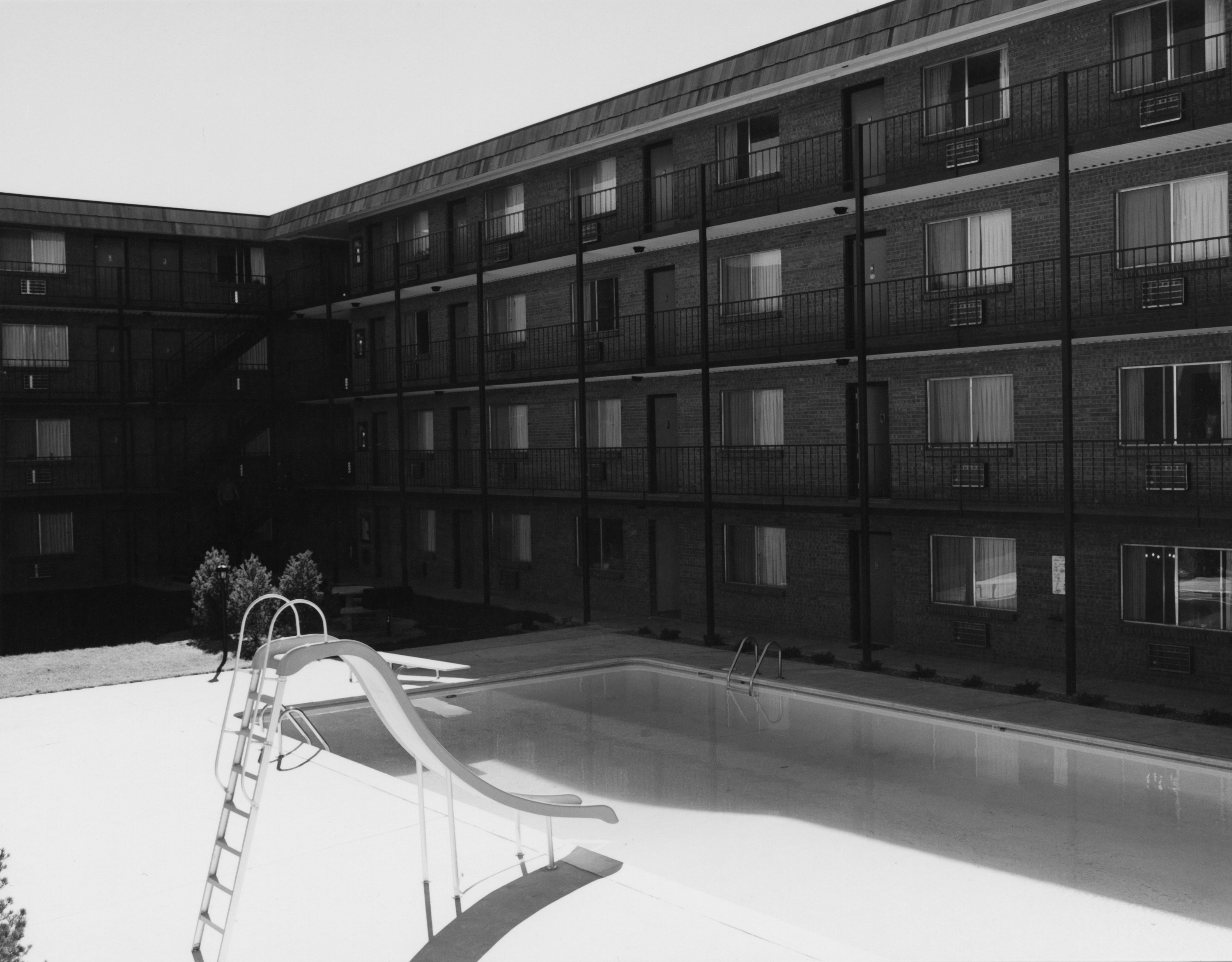 Black and white photograph of the exterior of an apartment complex with a pool