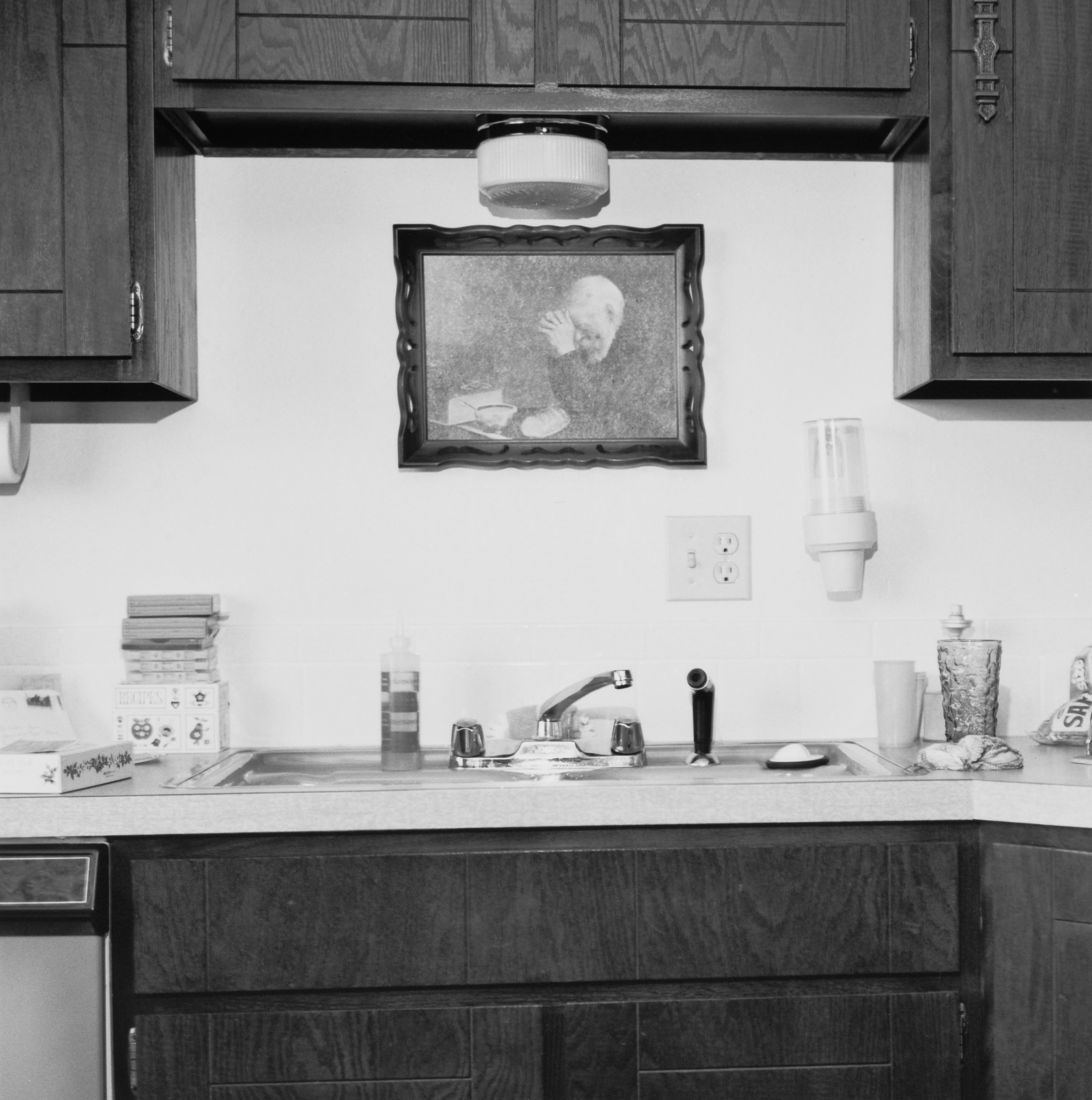 Black and white photograph of the interior of a kitchen sink with a painting above the sink