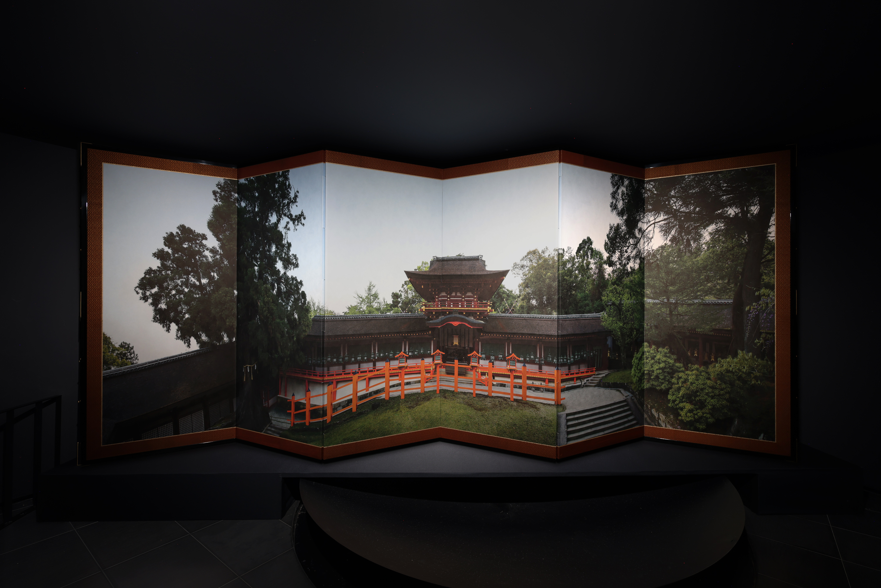 Color image of a folding screen on a black pedestal with a color photograph of the exterior of the Kasuga Grand Shrine at dawn