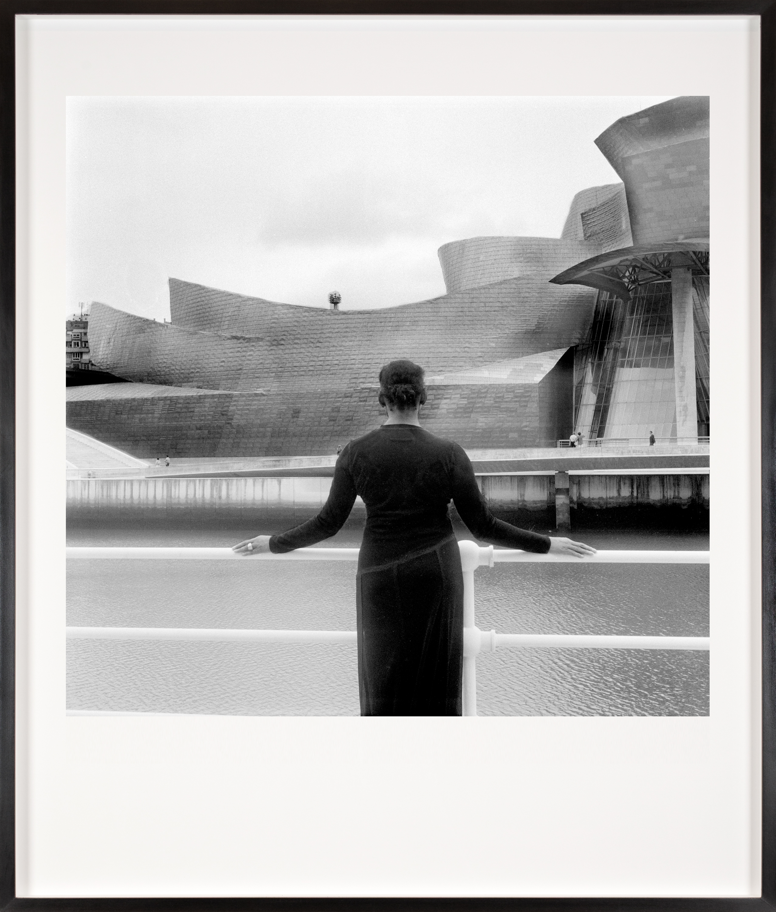 Black and white photograph of a figure in a black dress looking at the exterior of the Guggenheim Bilbao framed in black