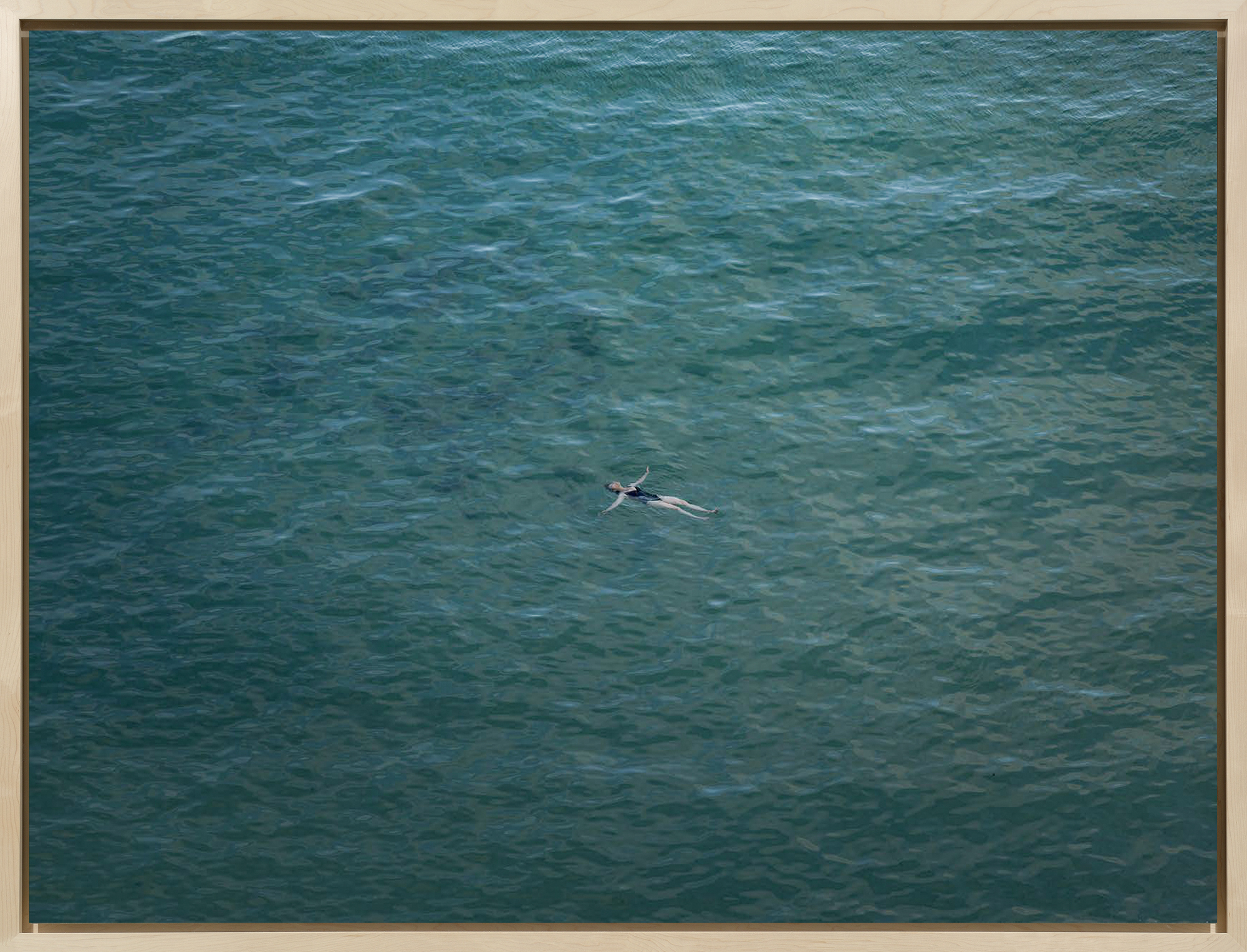 Color photograph of a figure floating in the middle of an ocean framed in bleached wood