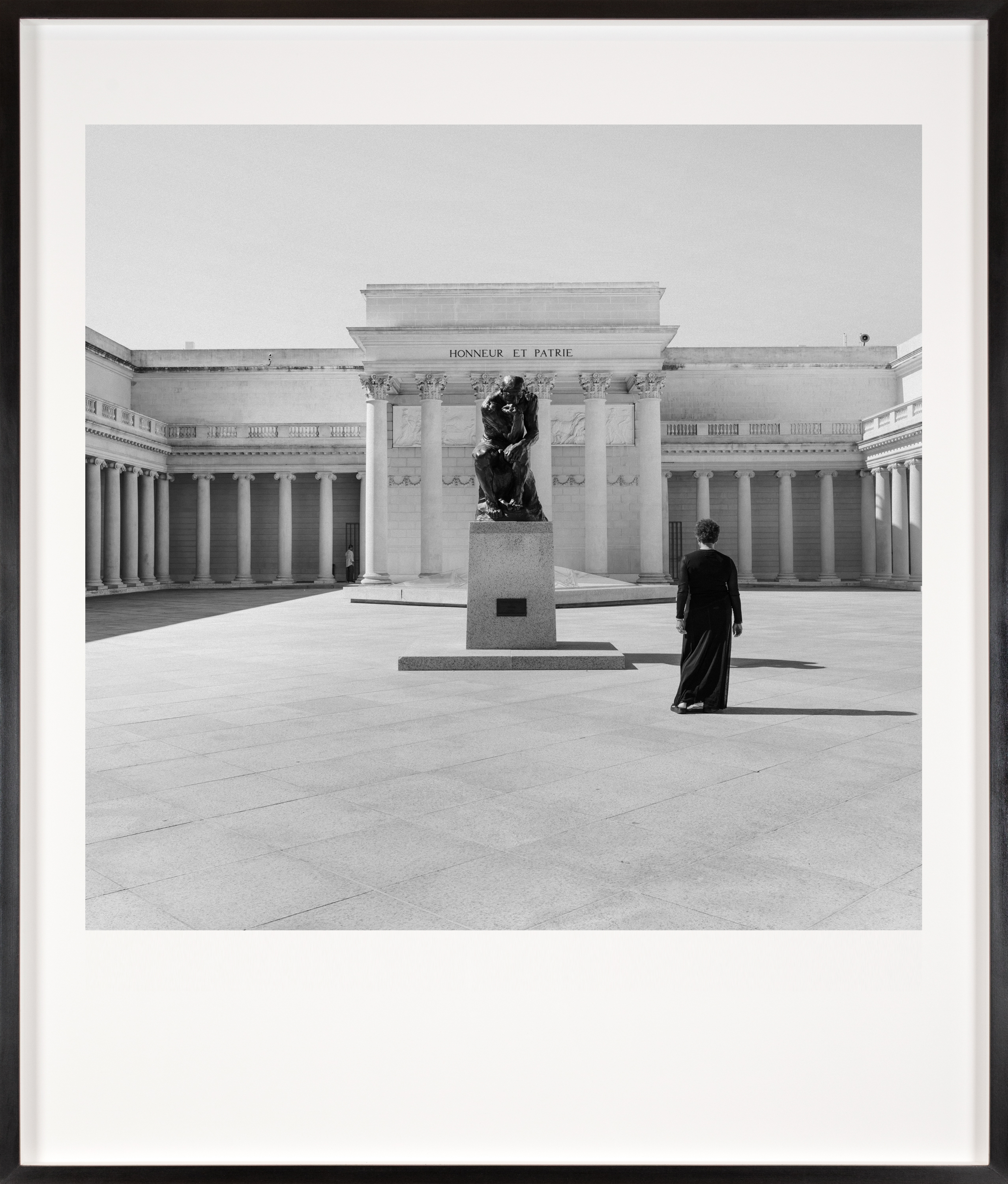 Black and white photograph of a figure in a black dress facing the exterior of a museum framed in black