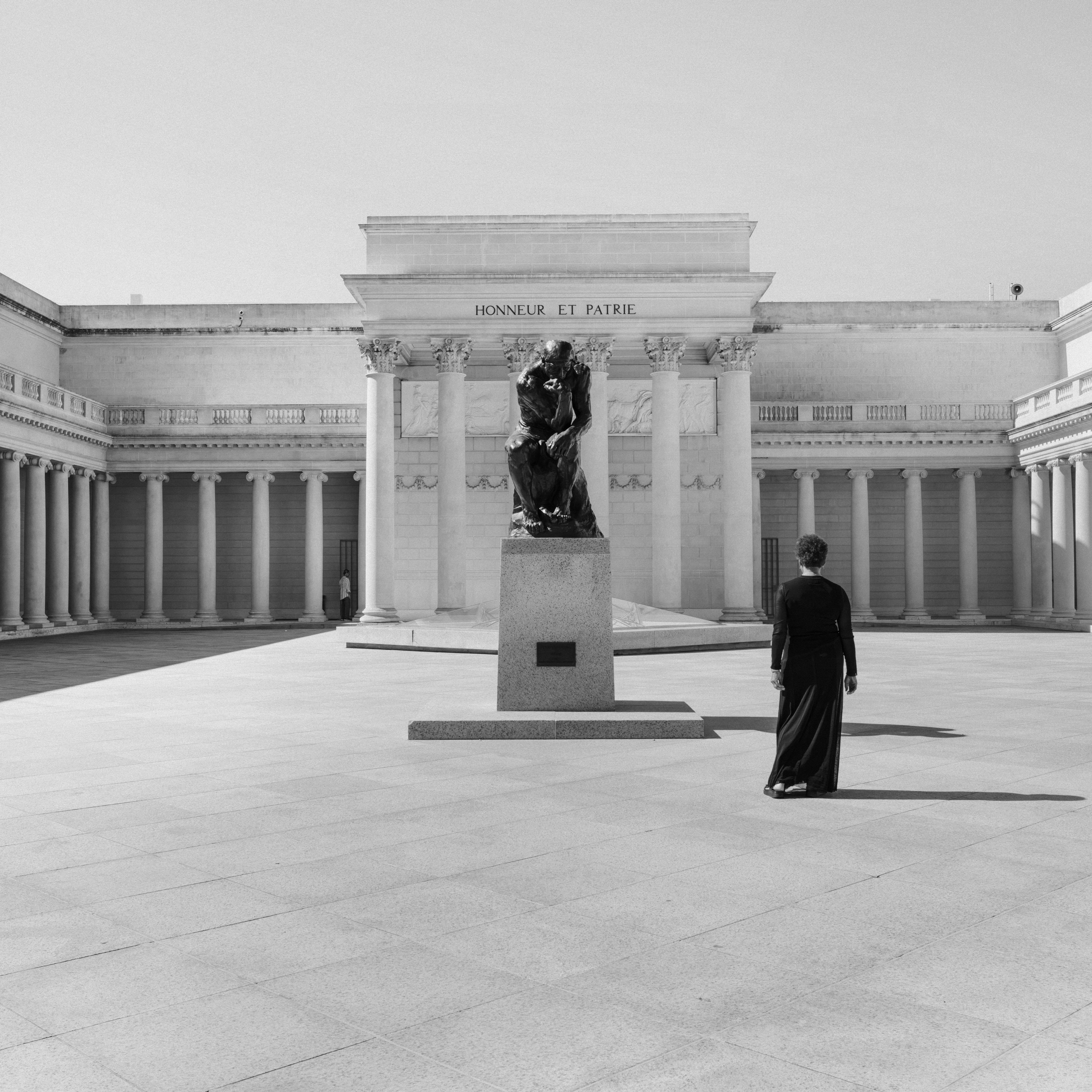 Black and white photograph of a figure in a black dress facing the exterior of a museum