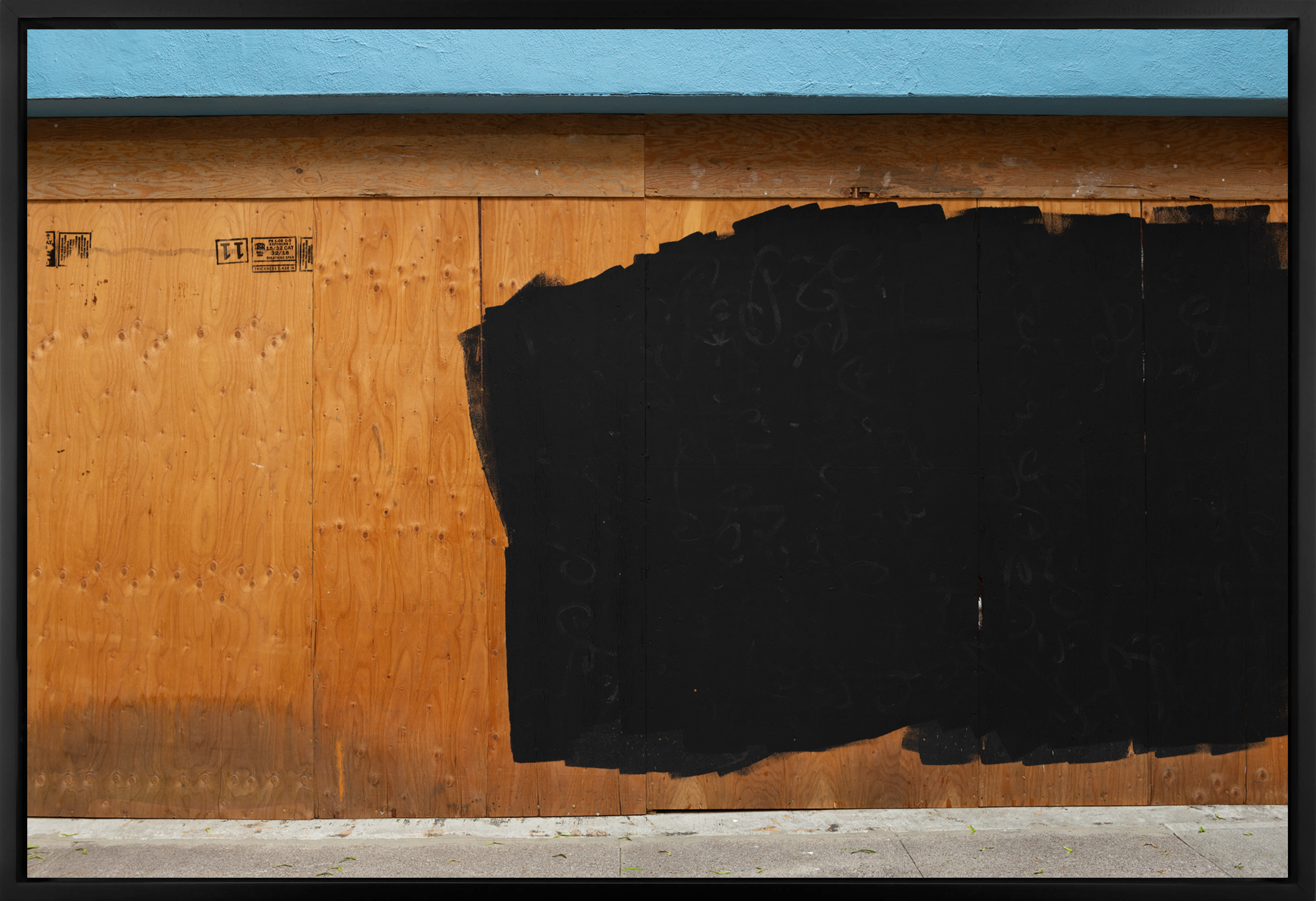 Color image of boarded up store front with paint splotches covering graffiti in black frame