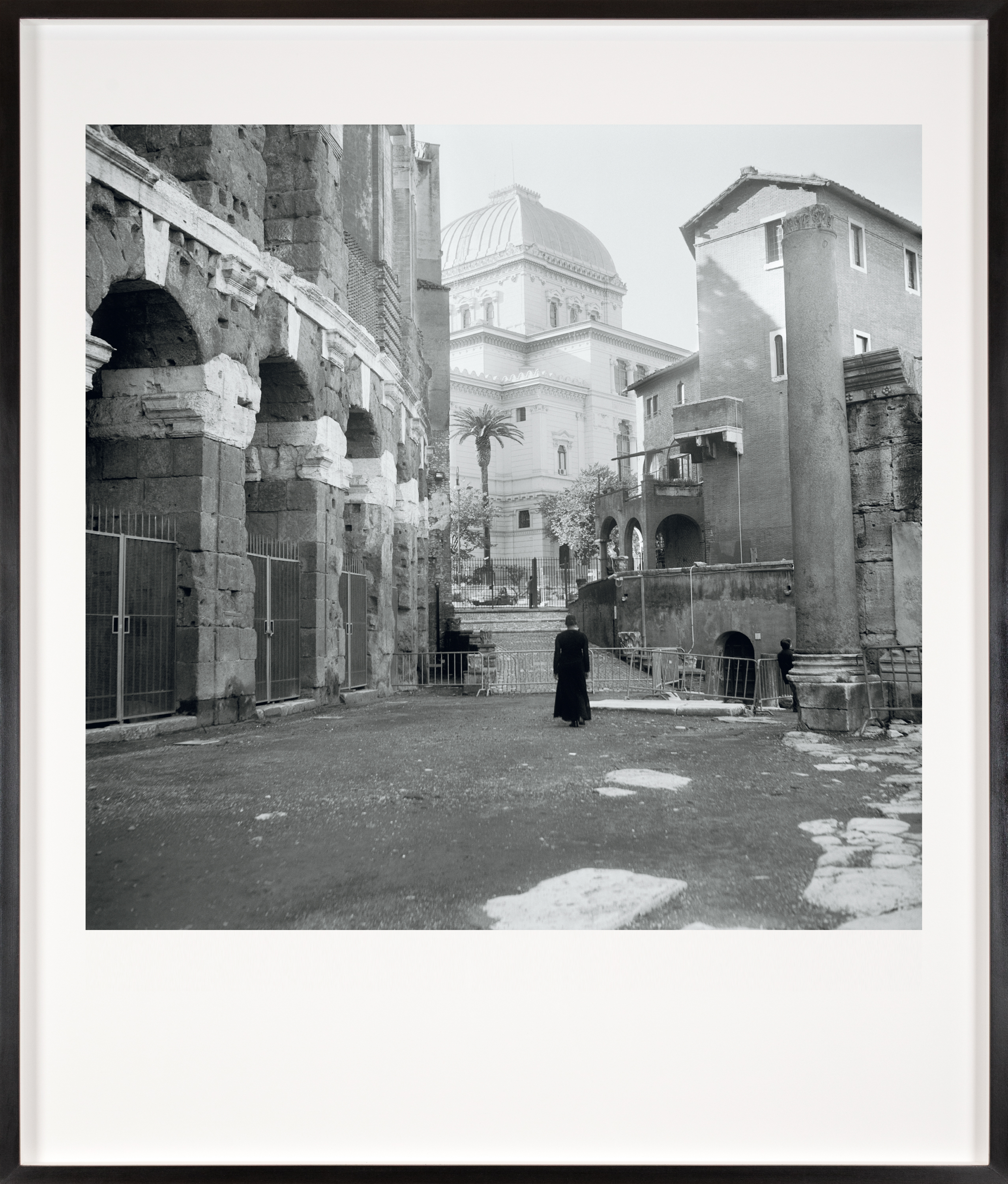 Black and white photograph of a figure in a black dress looking at the exterior of a temple framed in black