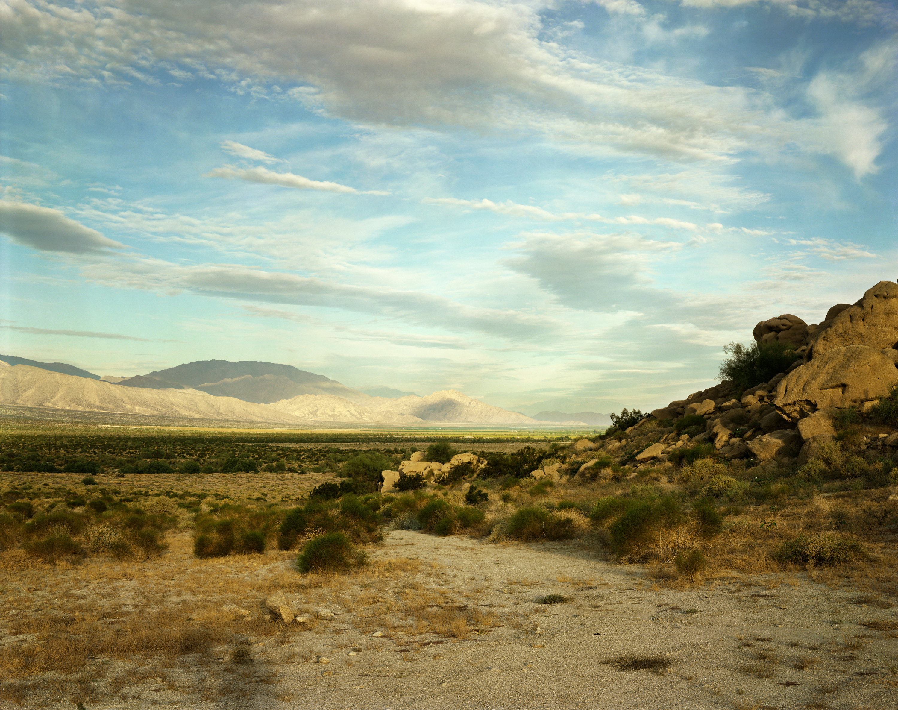 Color photograph of the desert during a sunny day with several clouds in the sky and the shadow of the photographer in the foreground